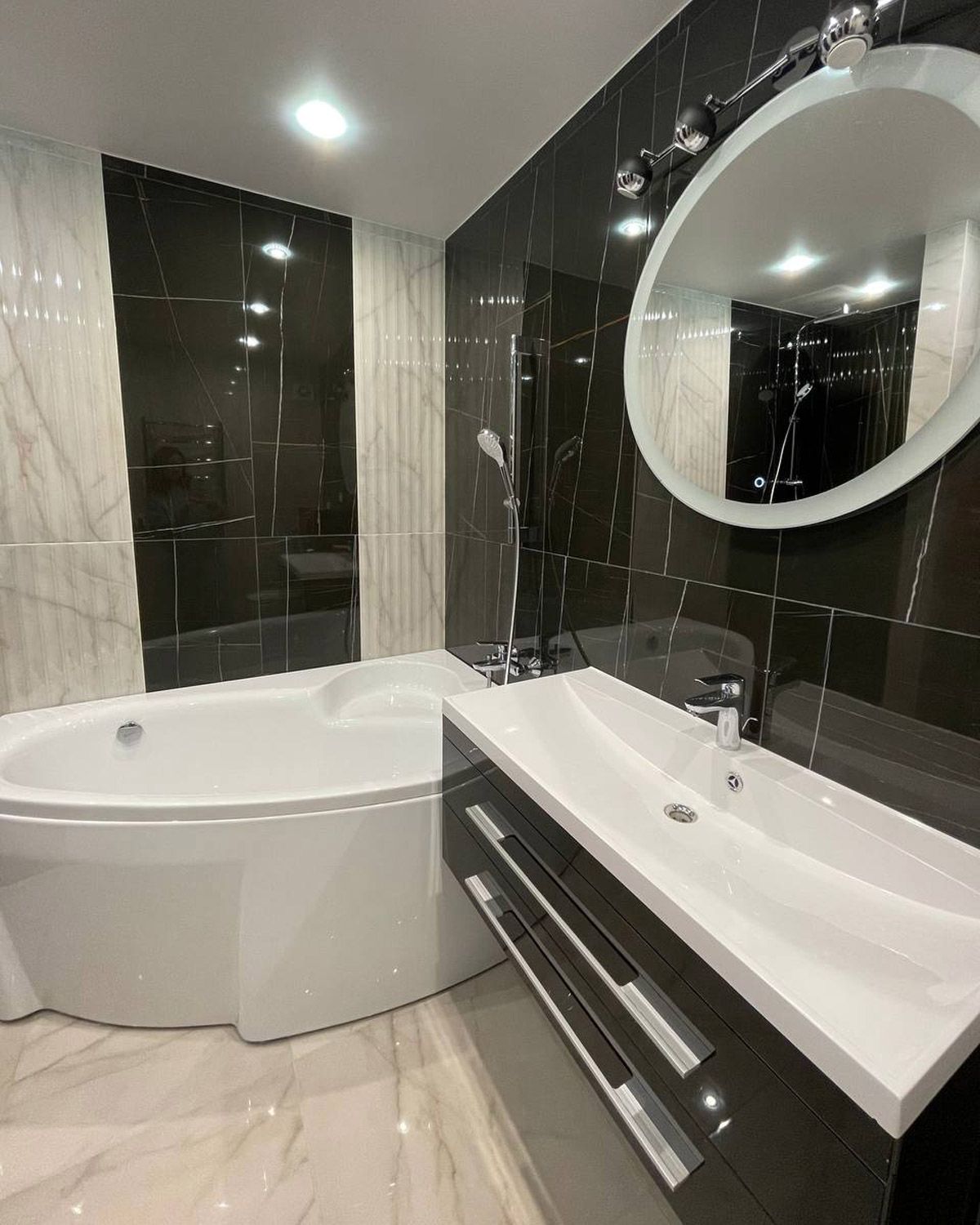 Remodeled bathroom with dark wall tile, vanity and tub