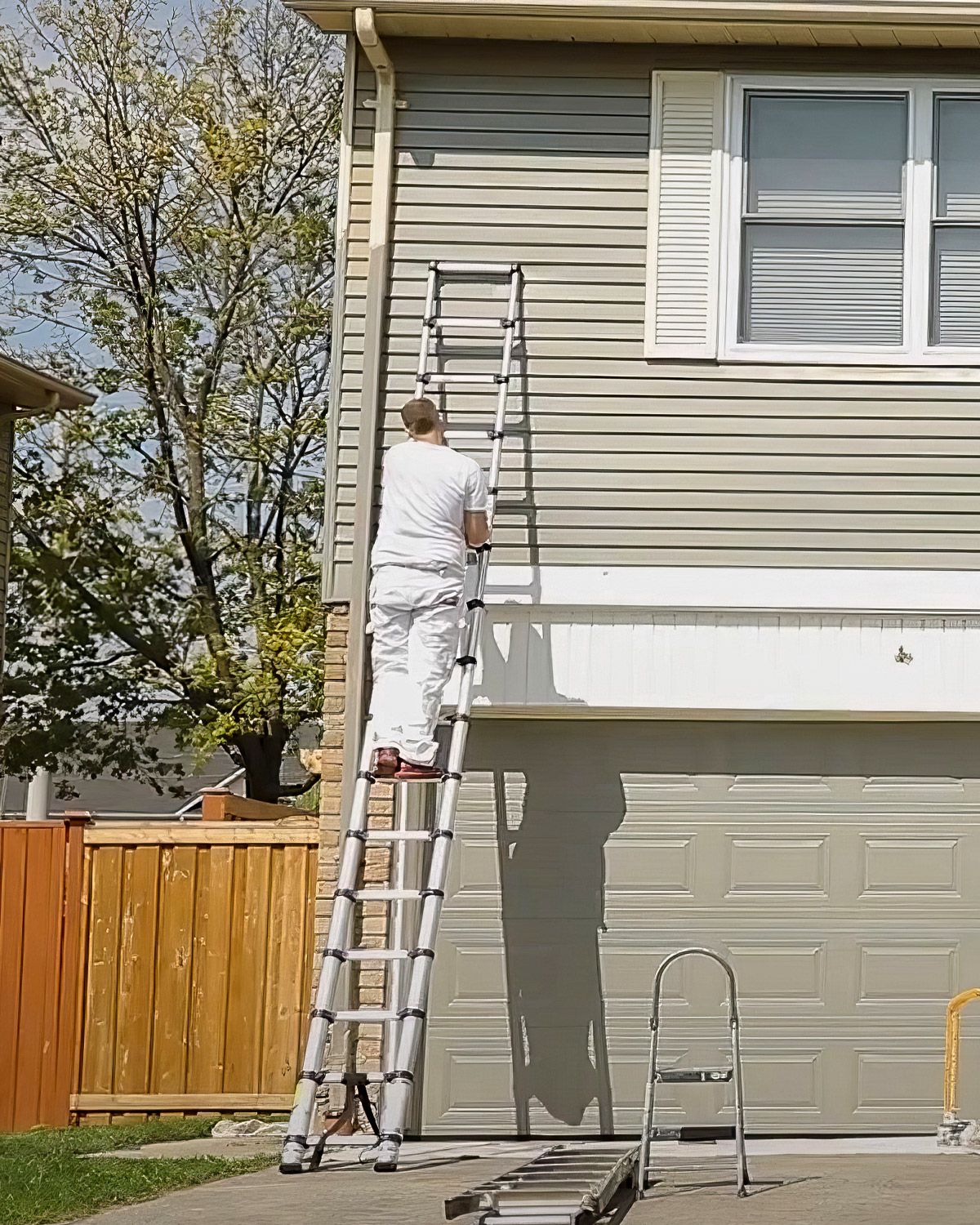 Painter on a ladder painting the siding of a two-story house