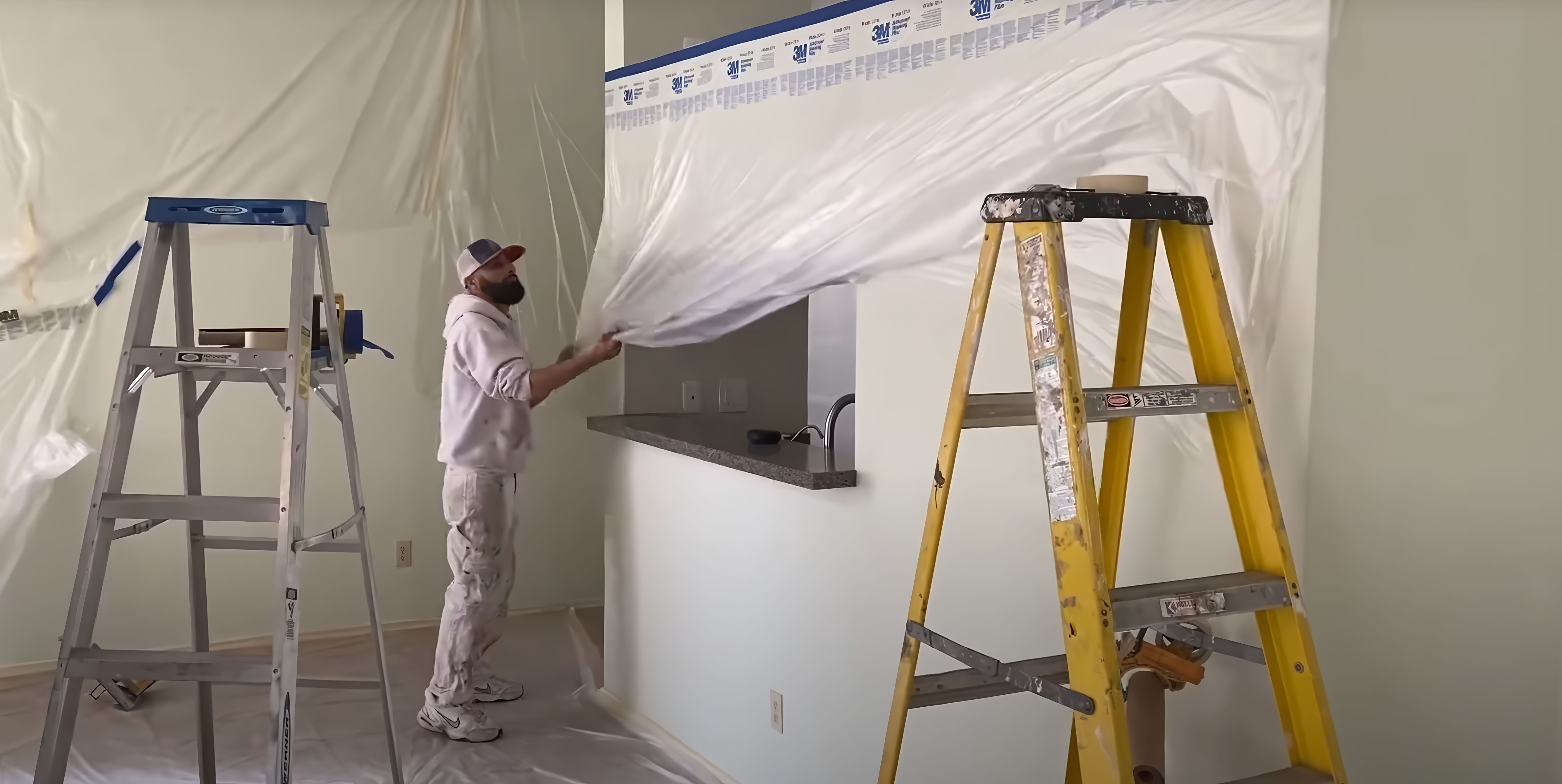 Painter masking kitchen cabinets and the floor in plastic before spraying