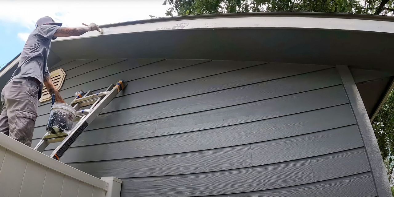 Painters on ladders painting the siding of a house