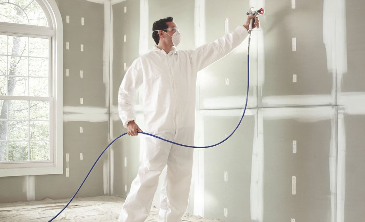 Painter in white coveralls spraying a wall with an airless sprayer