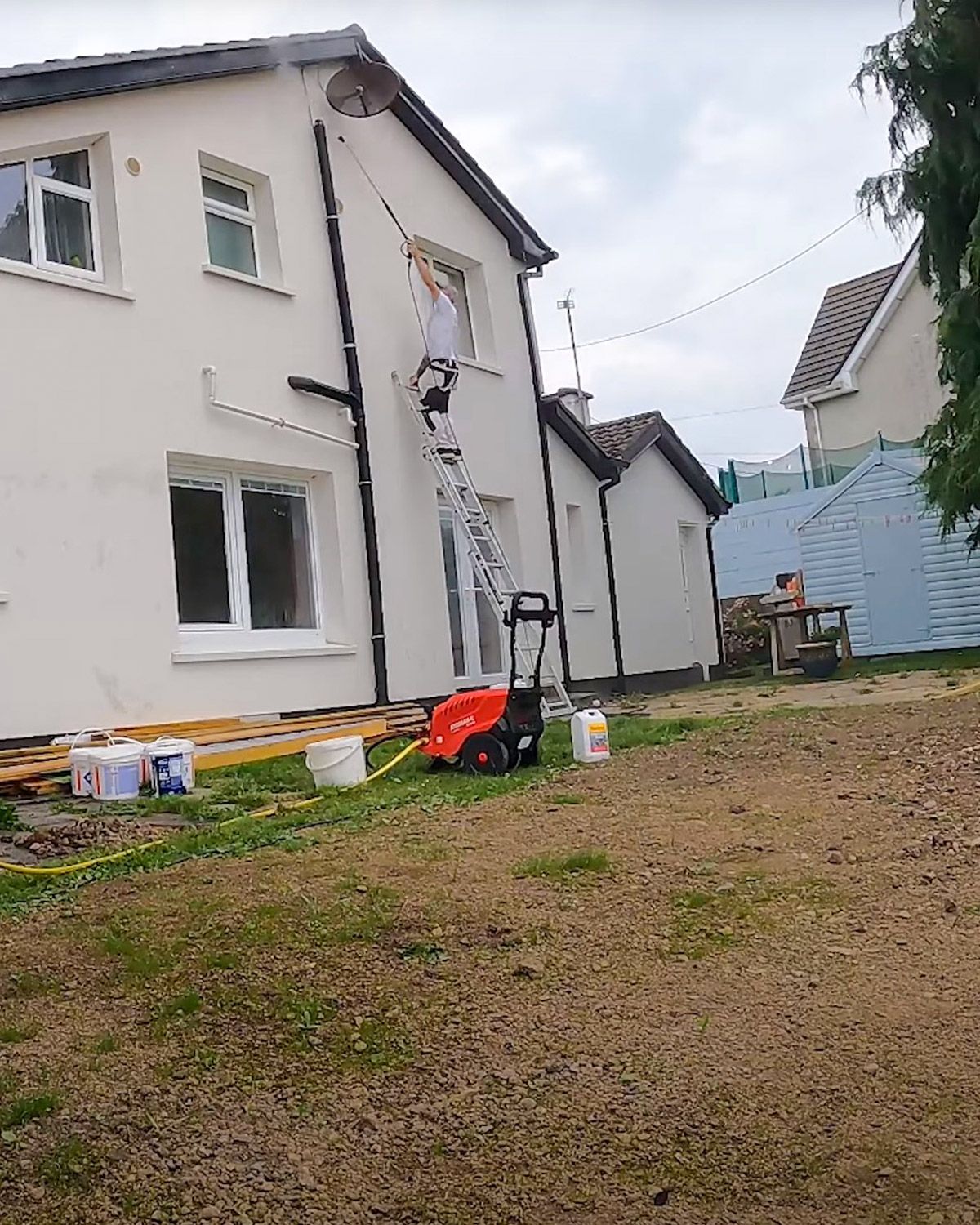 Crew member on a ladder pressure washing the upper wall of a house