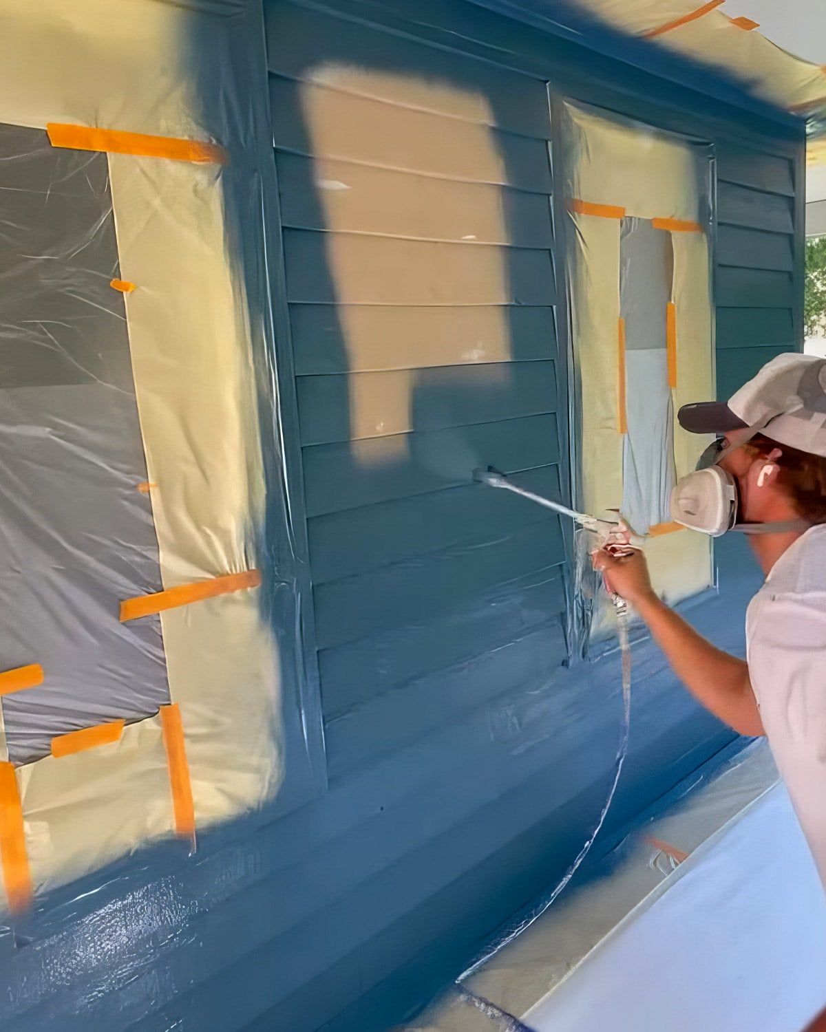 Painter spraying siding after masking the windows