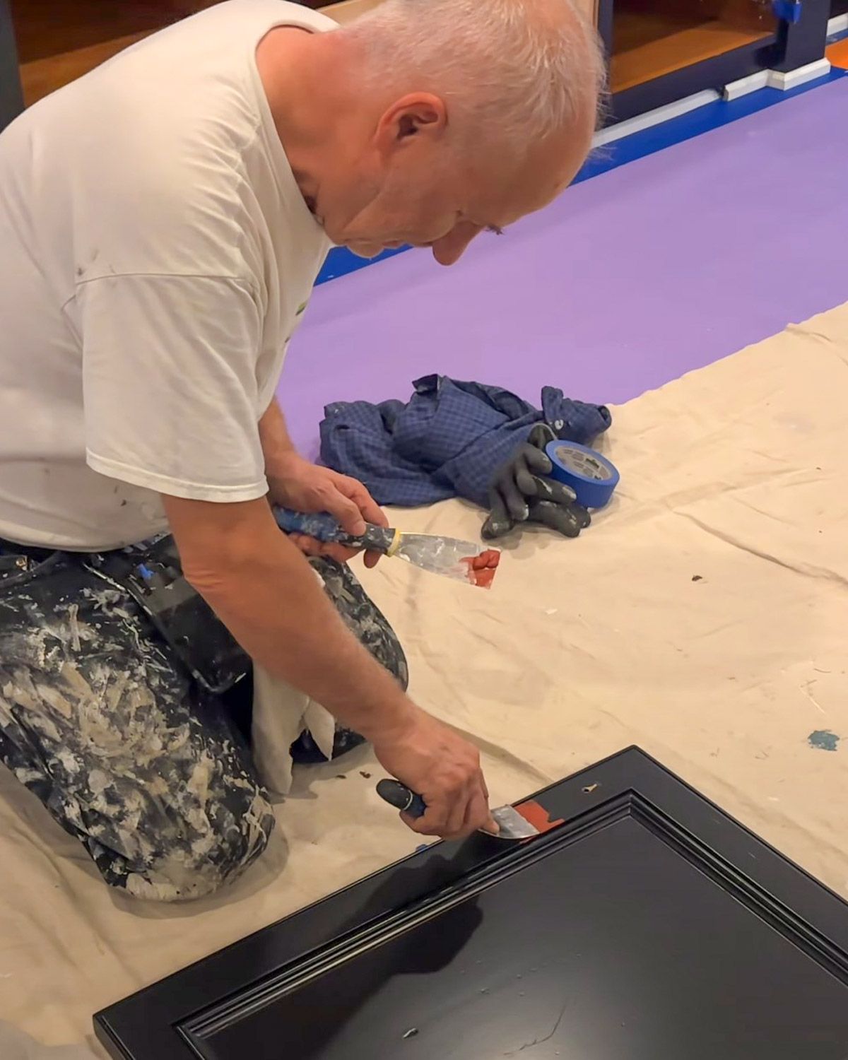 Painter filling old hardware holes in a cabinet door on a drop cloth