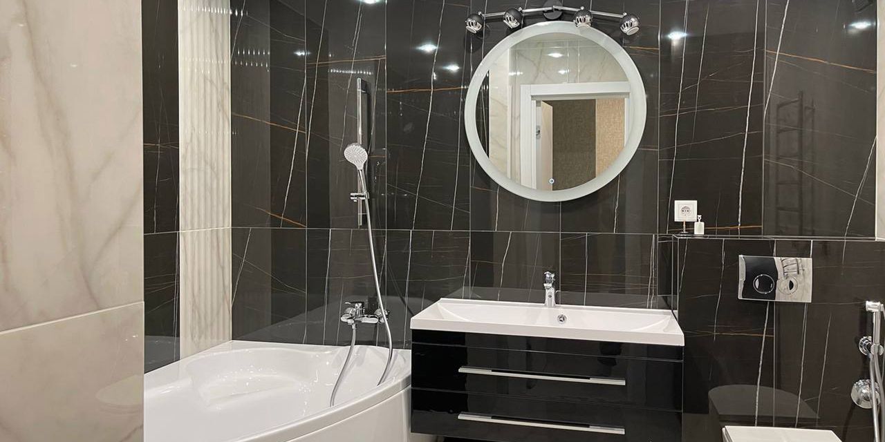 Finished bathroom with dark marble-look tile, round mirror, vanity and corner tub