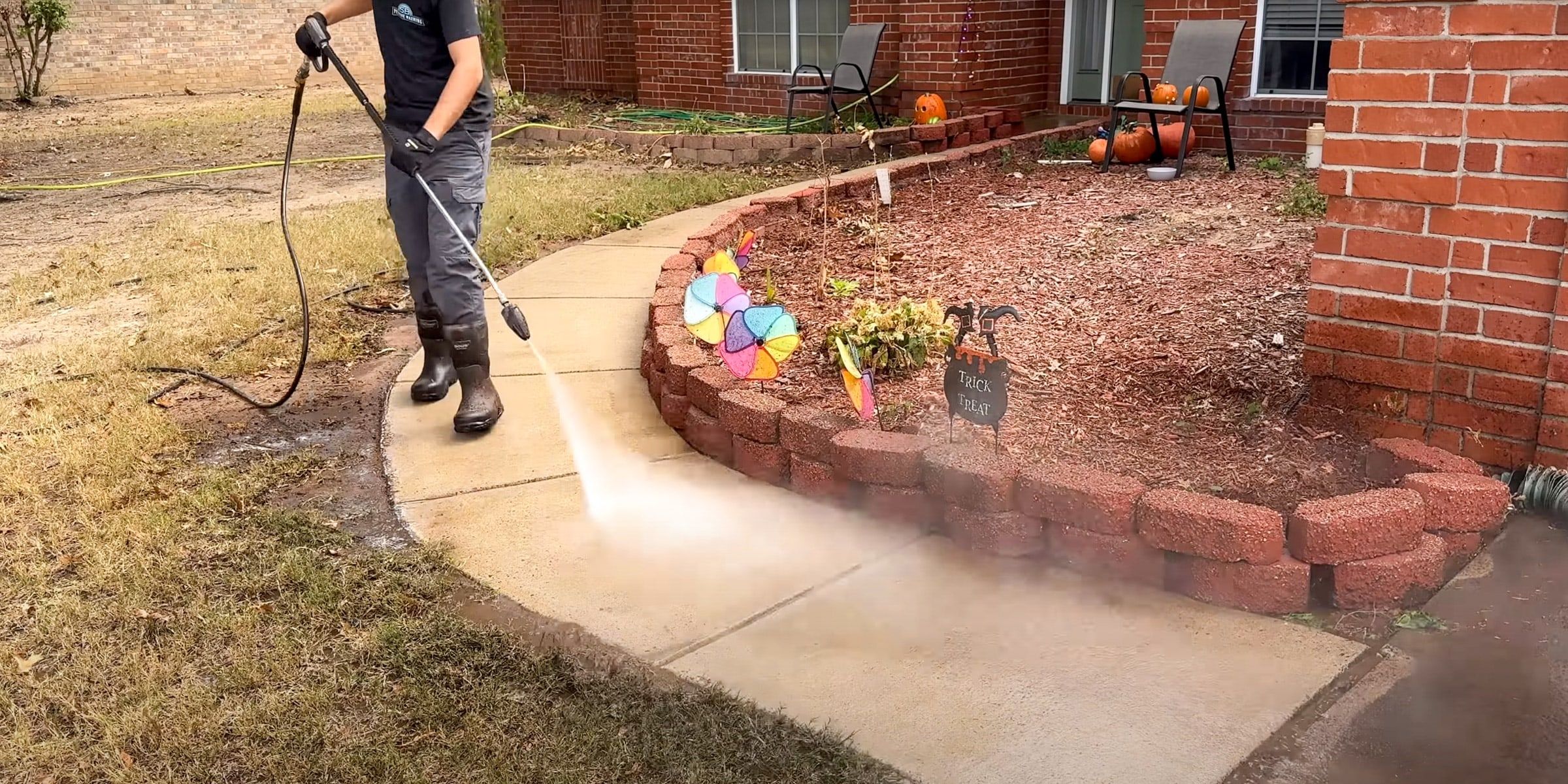 Crew member pressure washing a walkway next to a brick flower bed