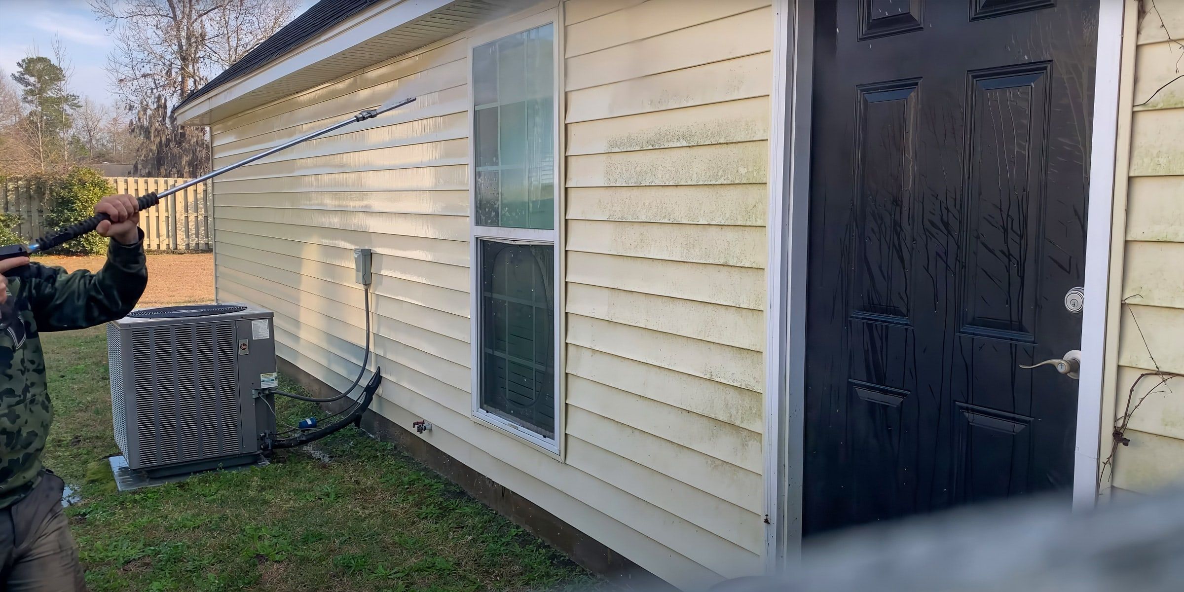 Pressure washing house siding beside the AC unit