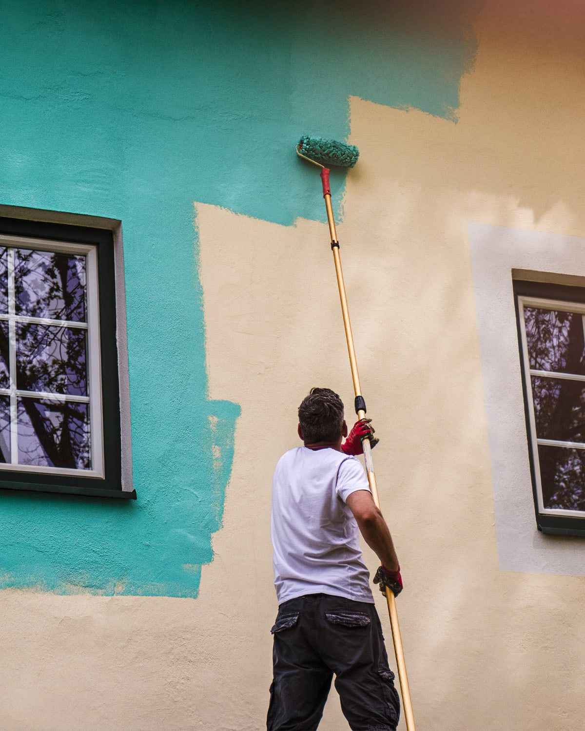 Painter rolling an exterior wall with an extension pole