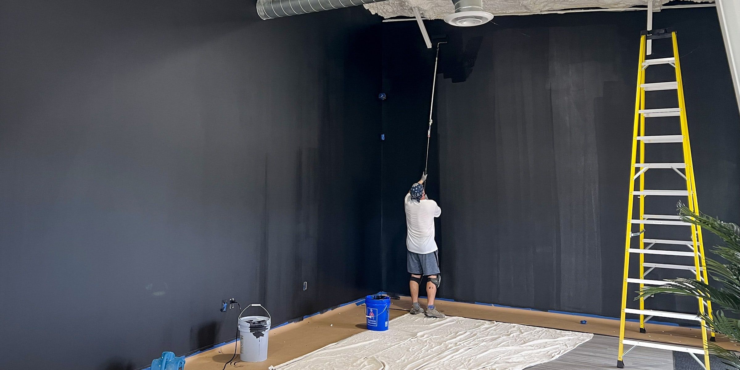 Painter rolling a tall warehouse wall dark gray