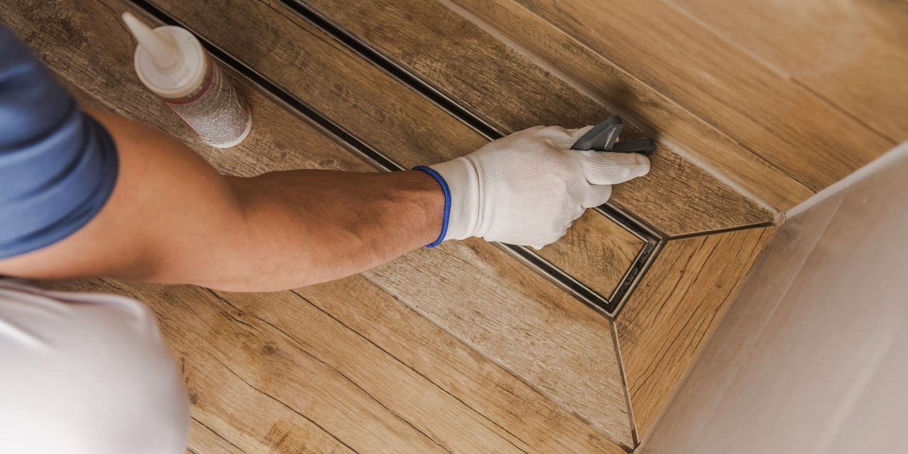 Installer sealing the edge of a linear shower drain in a wood-look tile floor