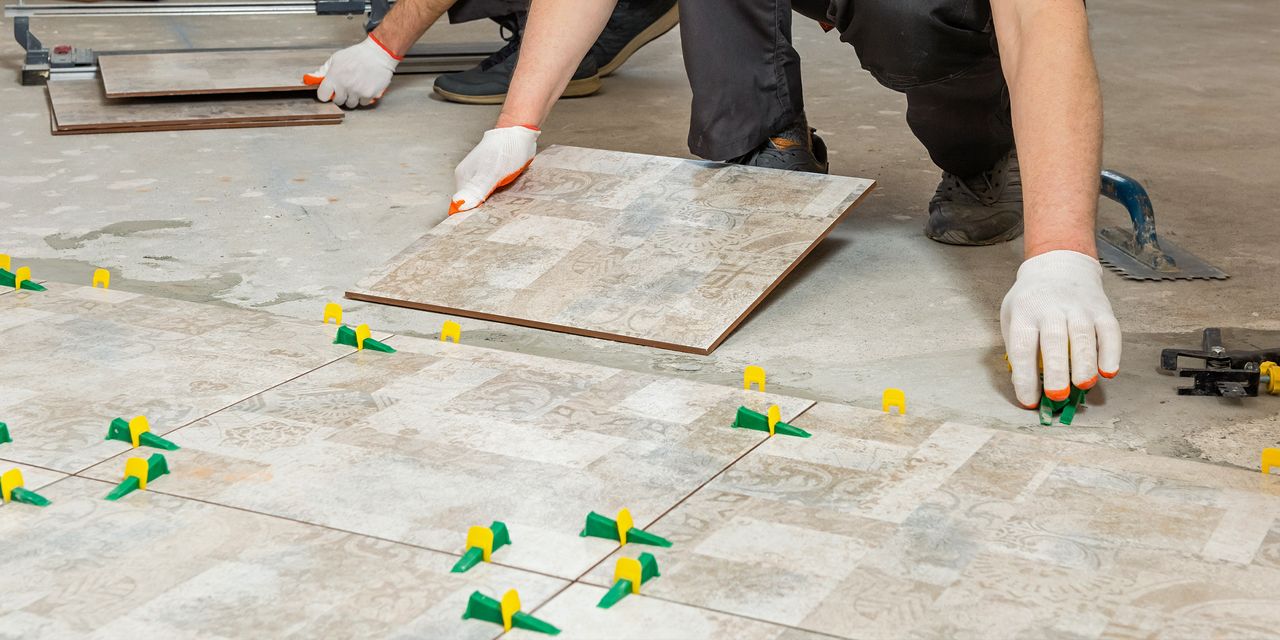 Installers laying large porcelain floor tiles with leveling clips