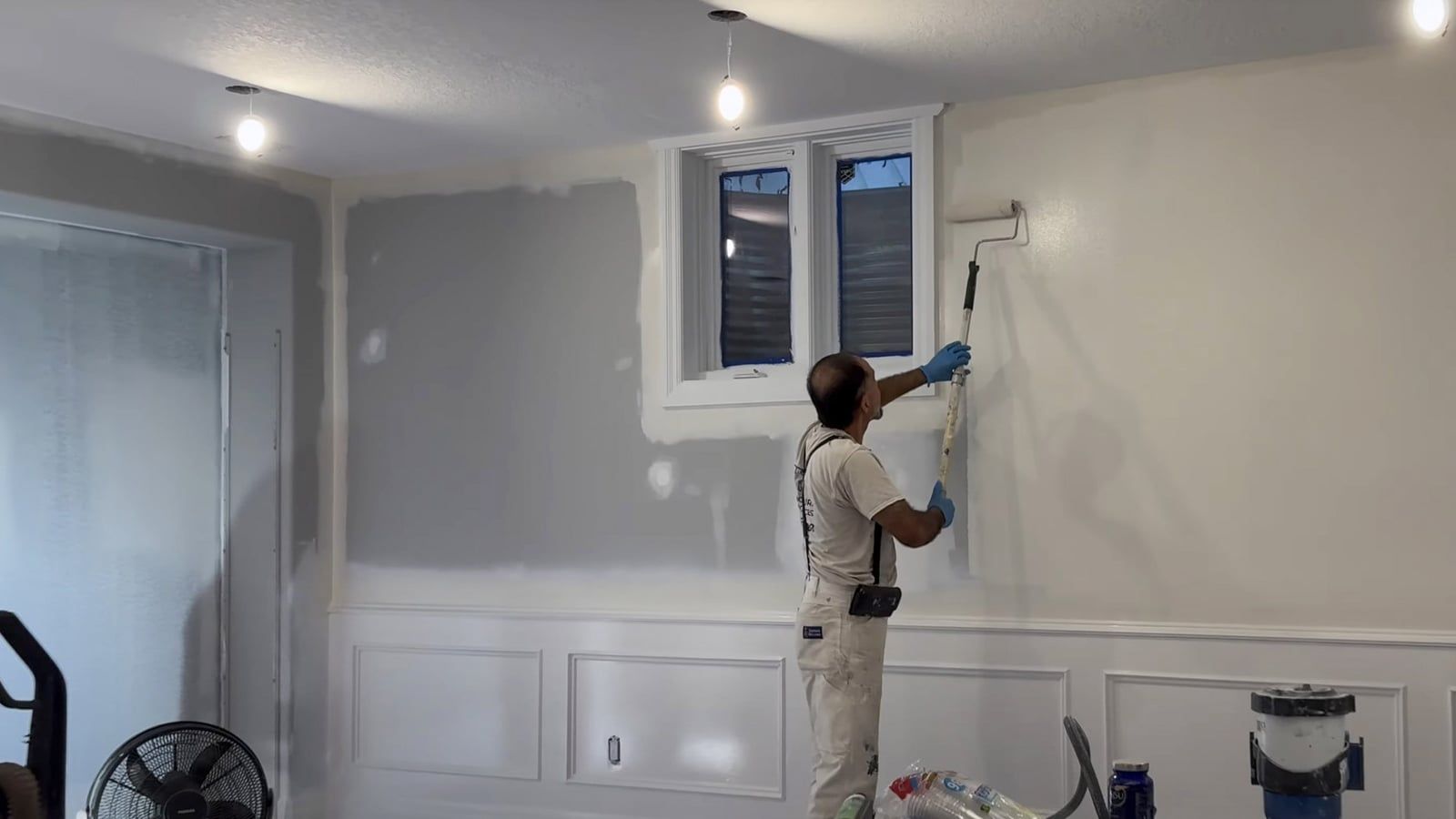 Painter on a ladder painting a room with paneled walls